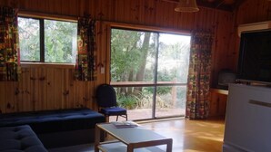 A cozy cabin with a sofa, a small table, and a refrigerator. Large windows offer a view of the outdoors.