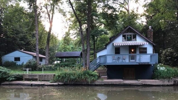 Una cabana a la vora d'un llac amb un balcó, envoltada d'arbres i una calma massa d'aigua.