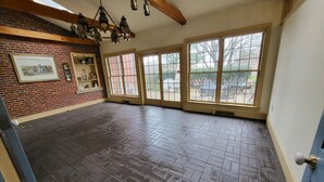 Una habitació àmplia amb paret de maó, grans finestres i sostre de fusta.