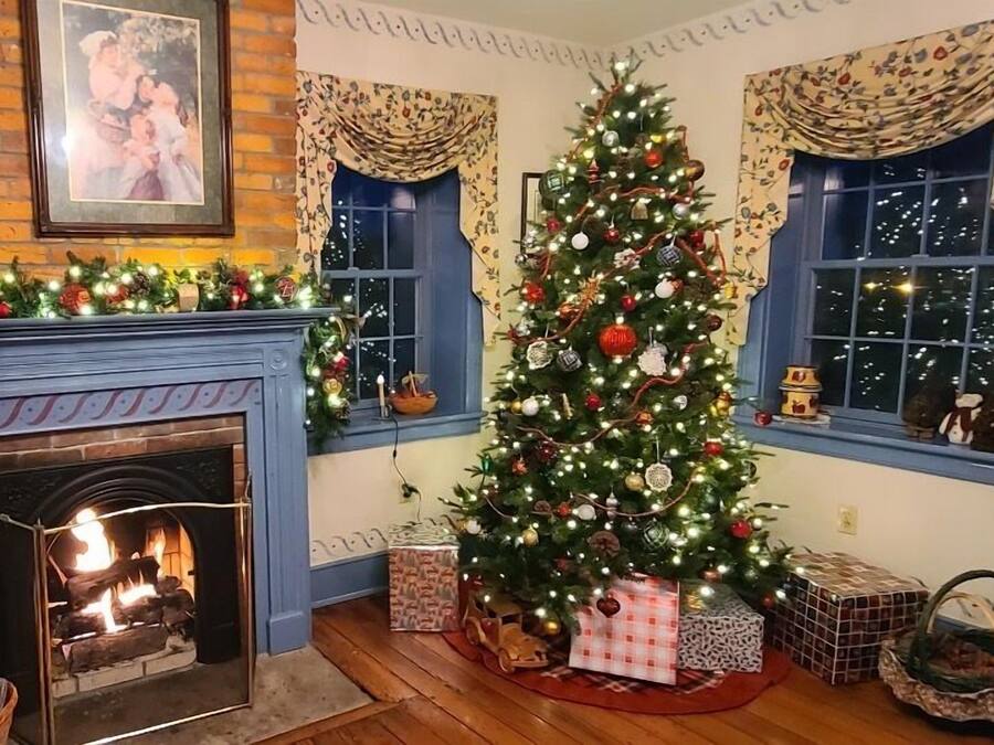 Una habitación acogedora con chimenea, un árbol de Navidad decorado y una ventana con cortinas.