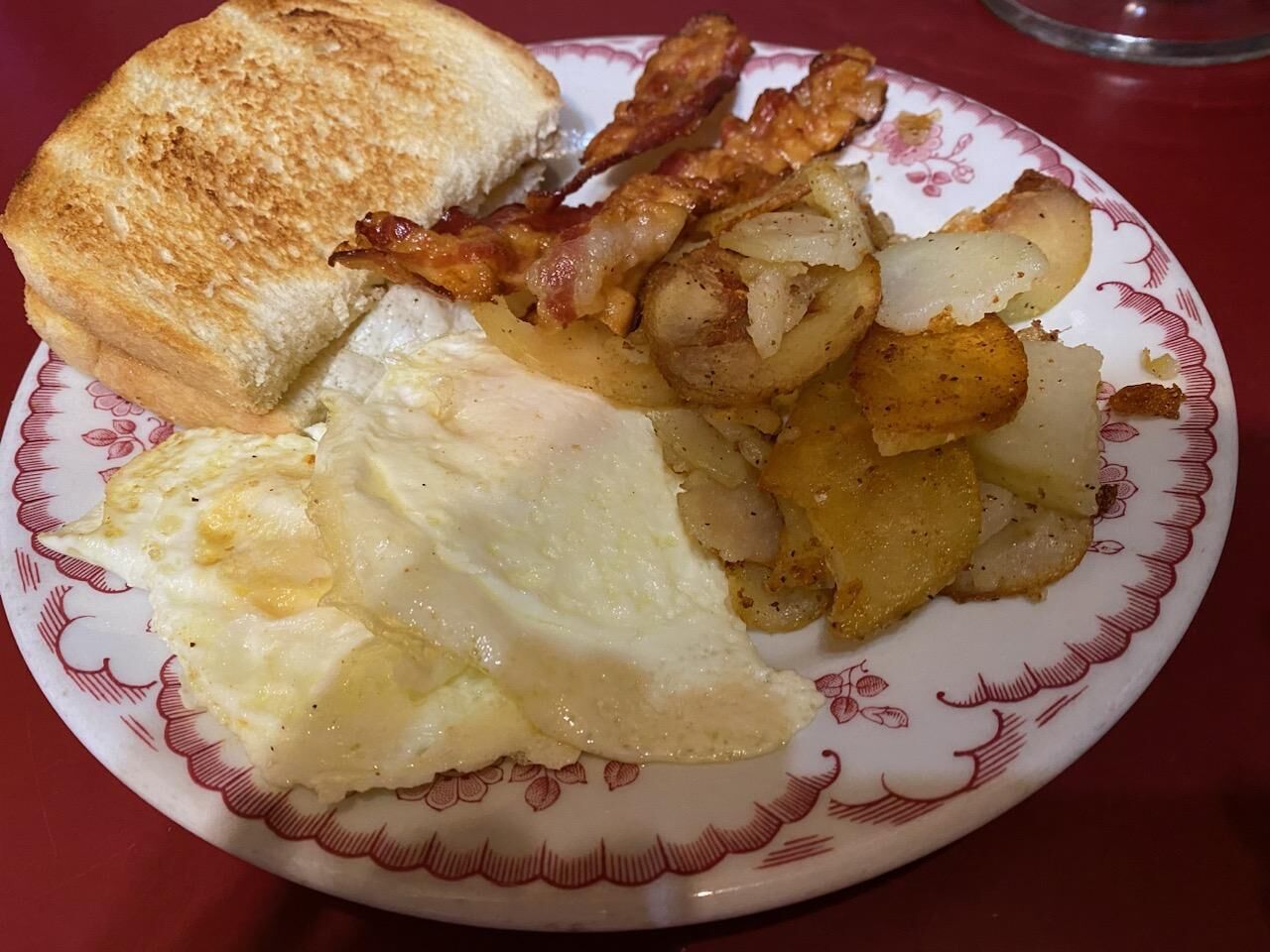 Un plato con tostadas, tocino, huevos y patatas.