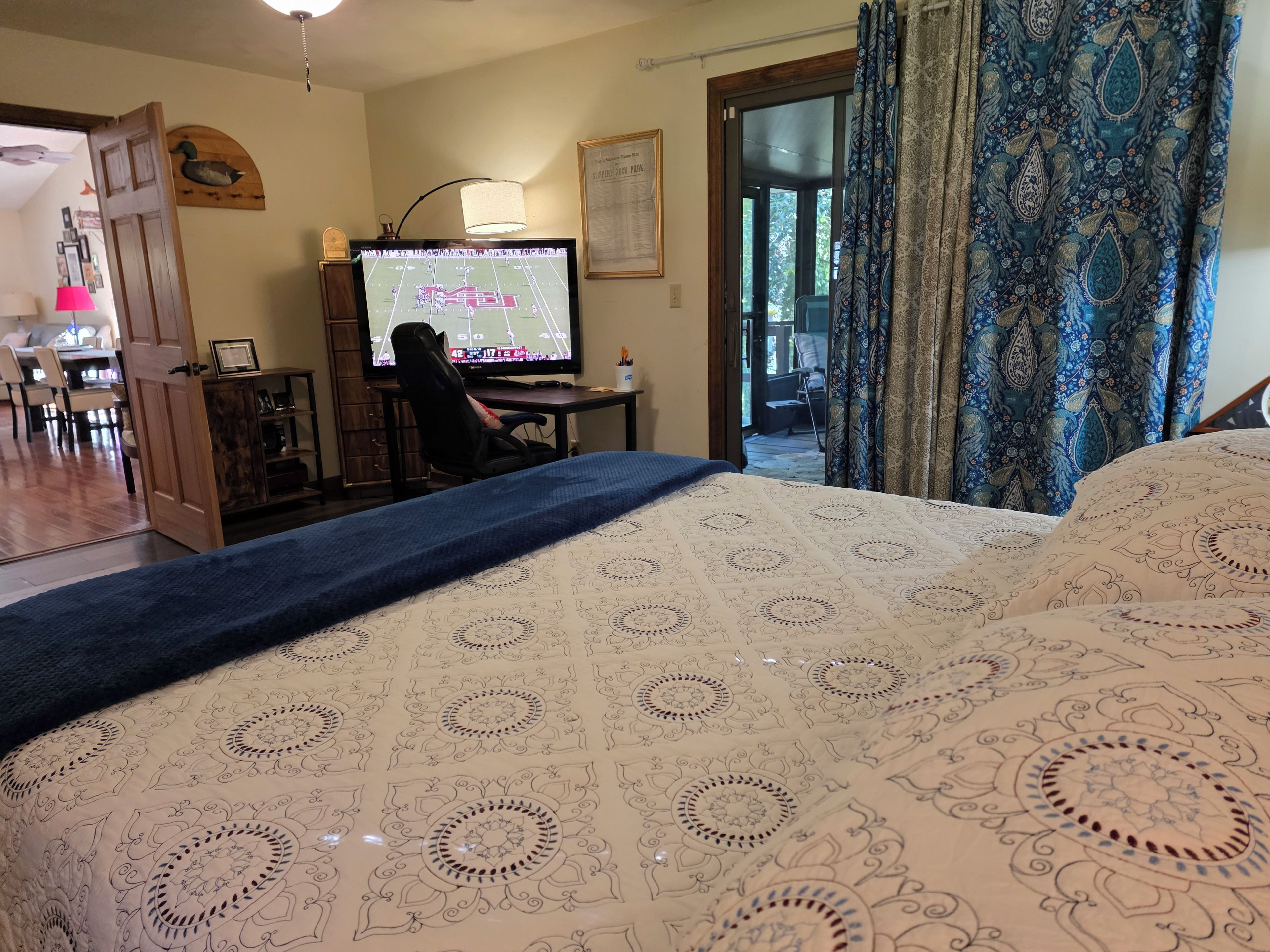 Una habitación con una cama, un escritorio con computadora, una silla y una puerta que da a otra habitación.