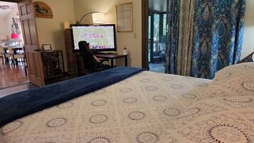 Una habitación con una cama, un escritorio con computadora, una silla y una puerta que da a otra habitación.