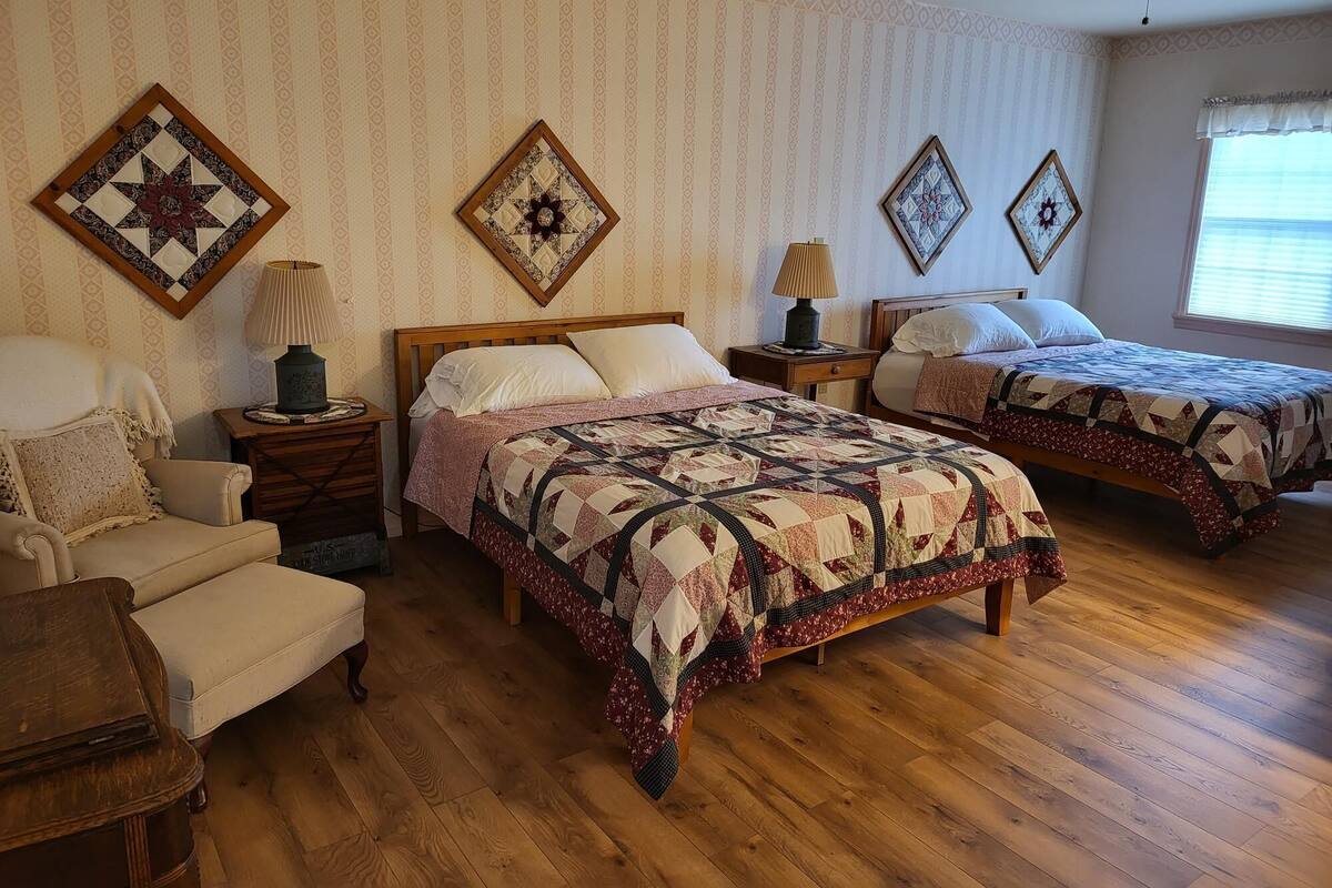 A bedroom with two beds, a chair, a nightstand, a lamp, and a ceiling fan.