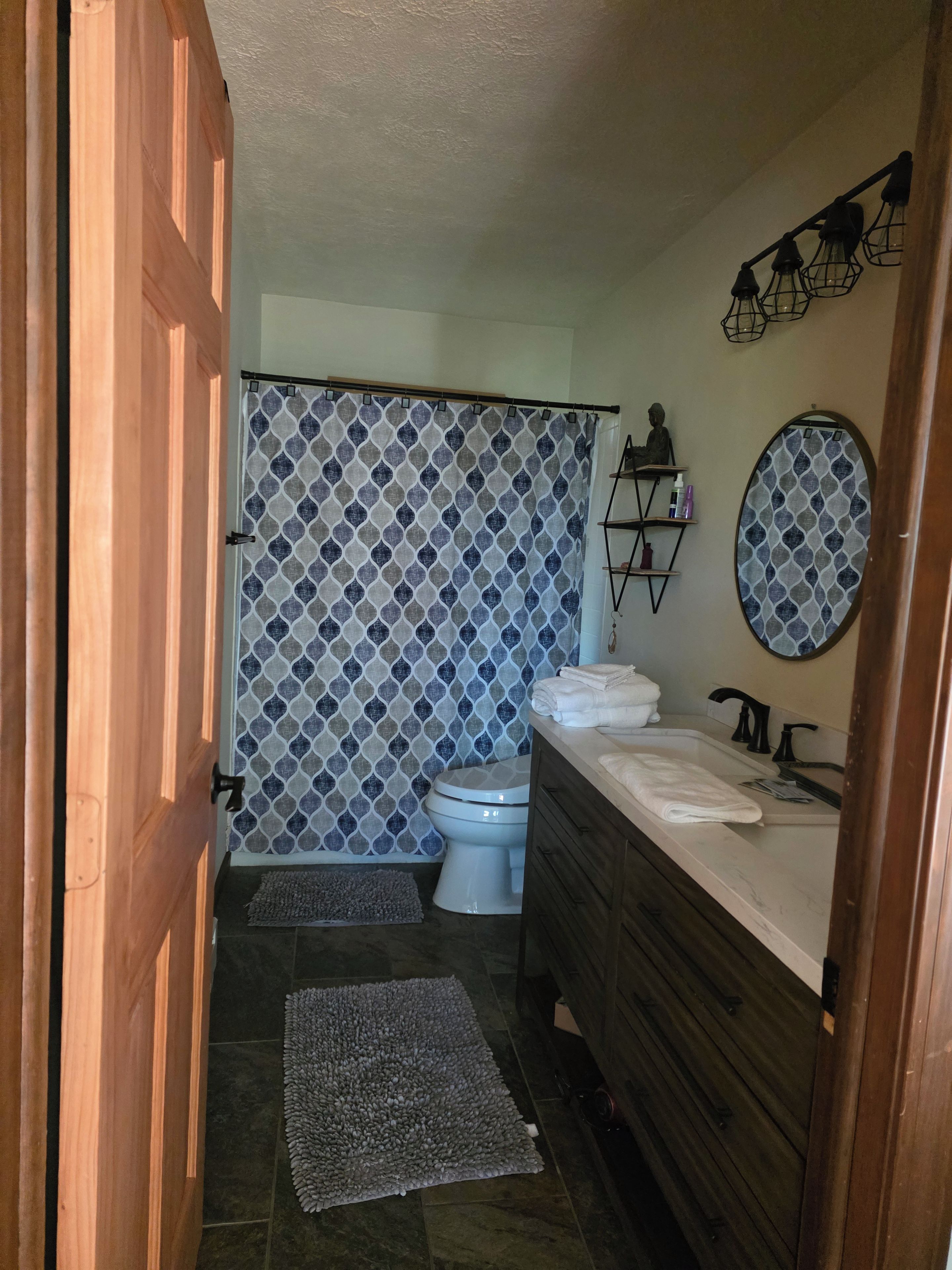 A bathroom with a shower curtain, toilet, sink, and wooden vanity.