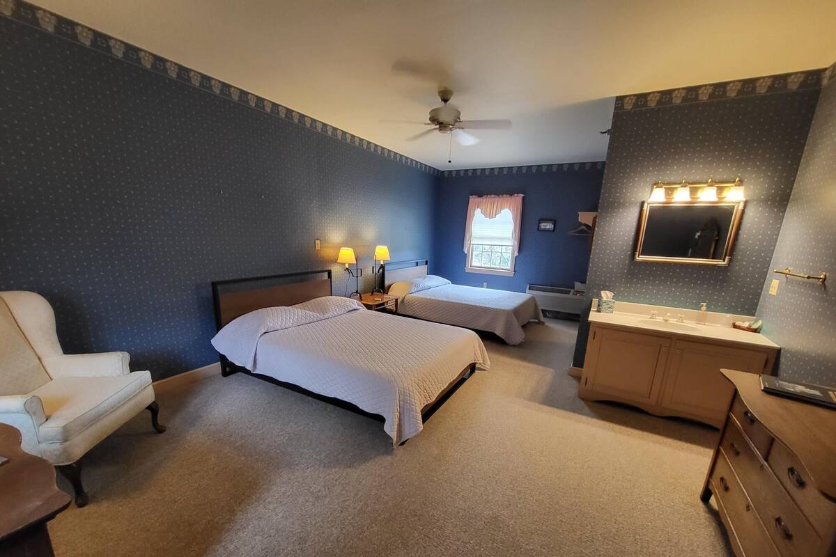 A bedroom with two beds, a chair, a dresser, a vanity, and a ceiling fan.