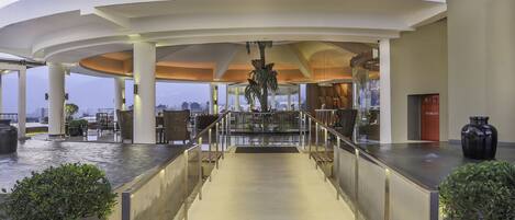 A spacious, modern lobby with a high ceiling, a central staircase, and a view of the cityscape.