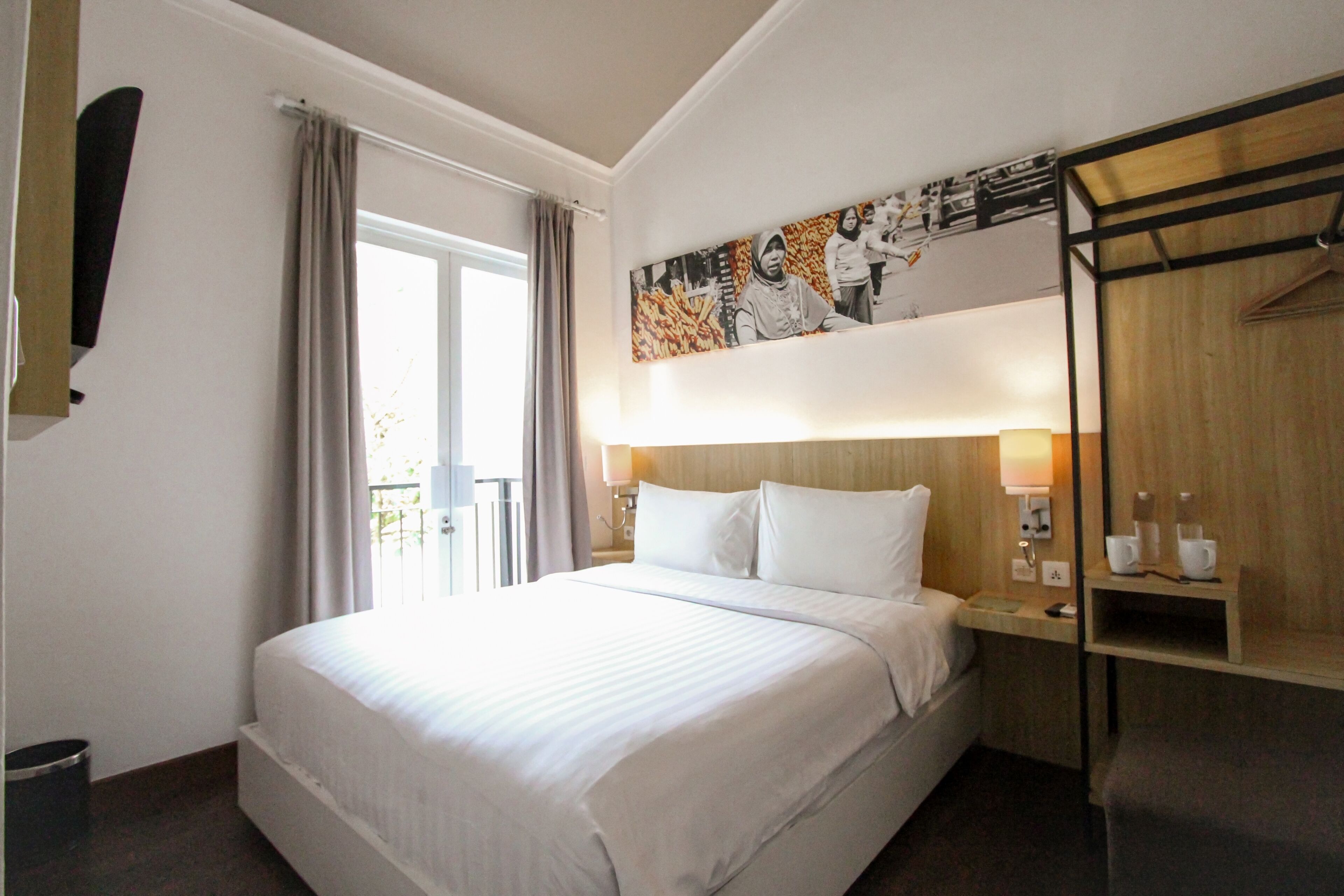 A hotel room with a large bed, a wardrobe, a bedside table with a lamp, and a window with curtains.