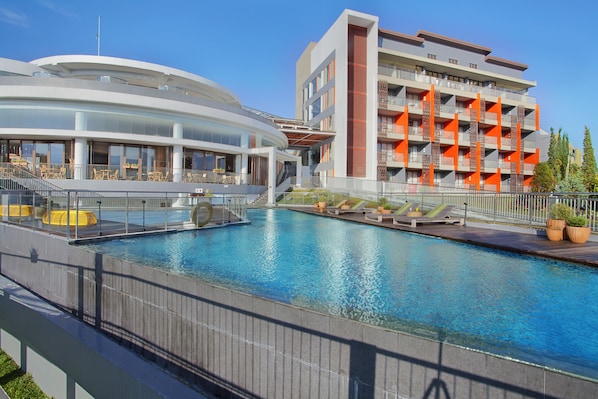 A modern hotel with a swimming pool, outdoor seating, and a multi-story building with balconies. - Pesona Alam Resort & Spa (Cisarua)