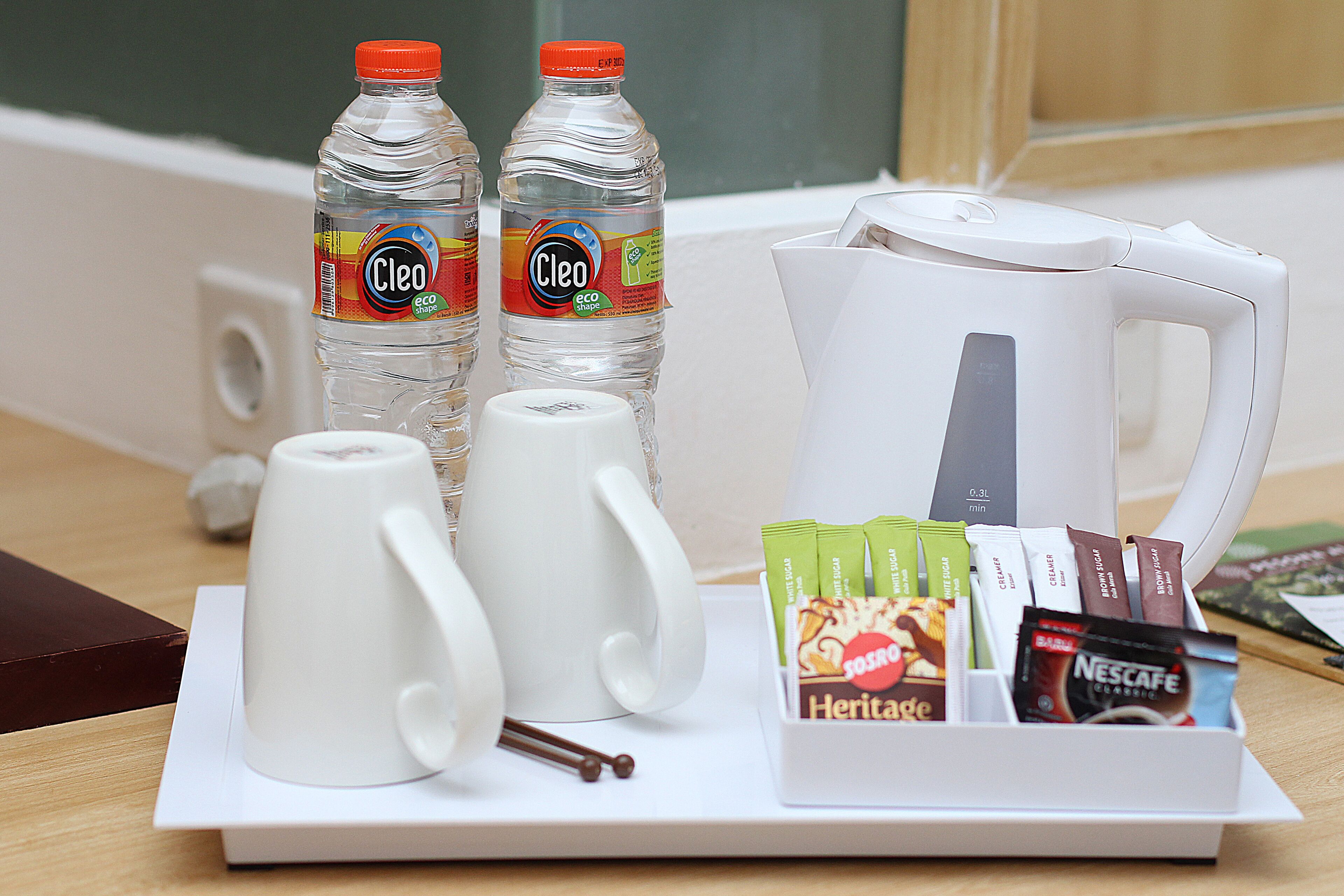 A tray with two bottles of water, a white electric kettle, two white mugs, and a selection of coffee and tea packets.