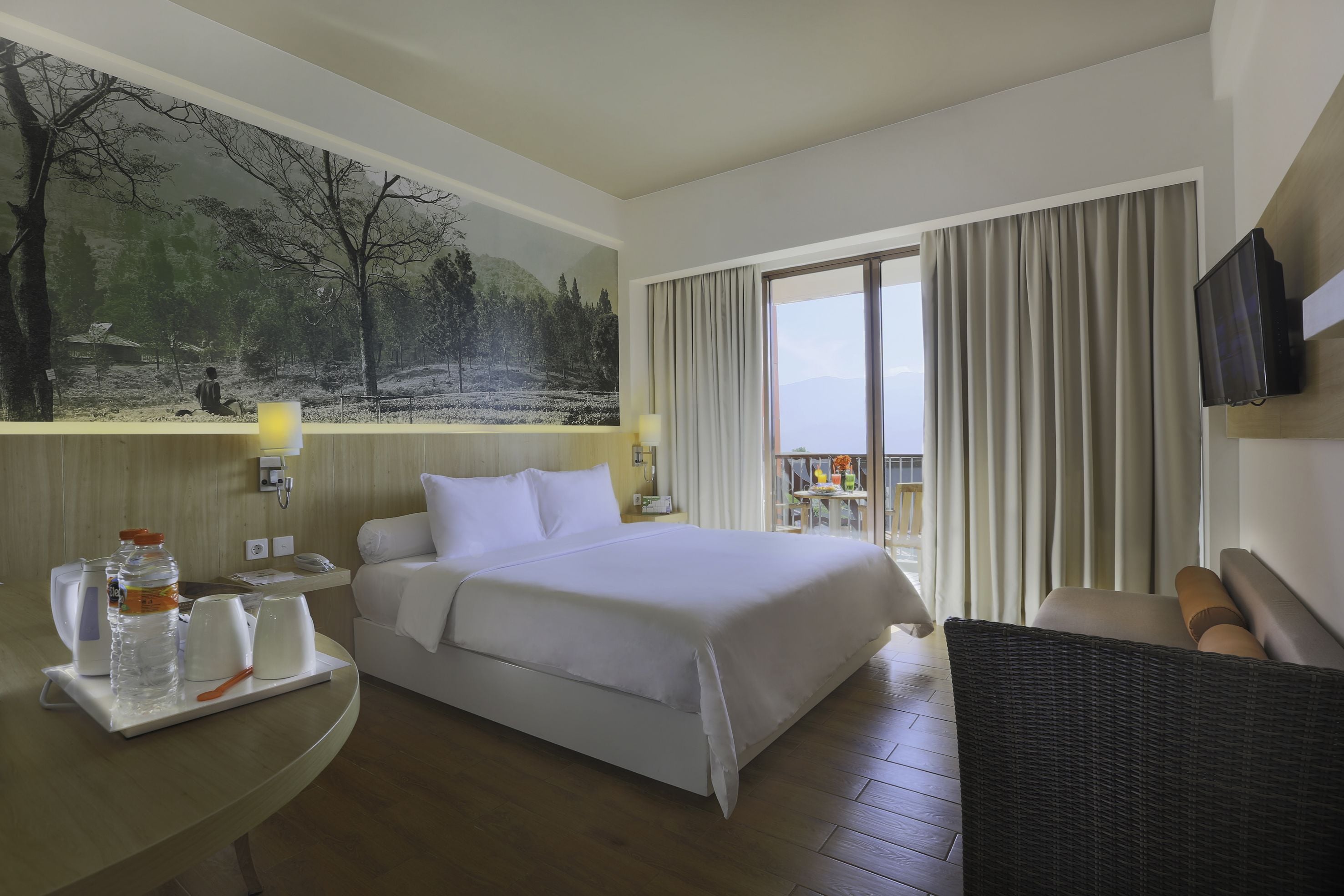 A hotel room with a large bed, a desk with a chair, a television, and a painting of a forest scene.
