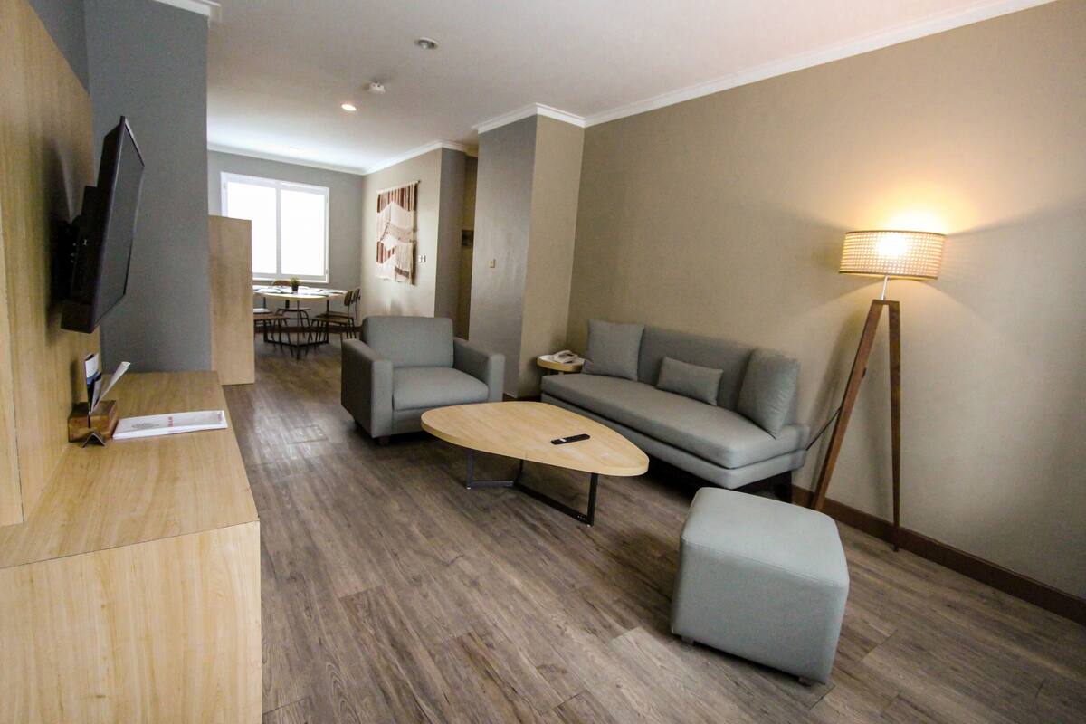 Uma sala de estar moderna com televisão de tela plana, mesa de centro de madeira, sofás cinzas e abajur de chão.