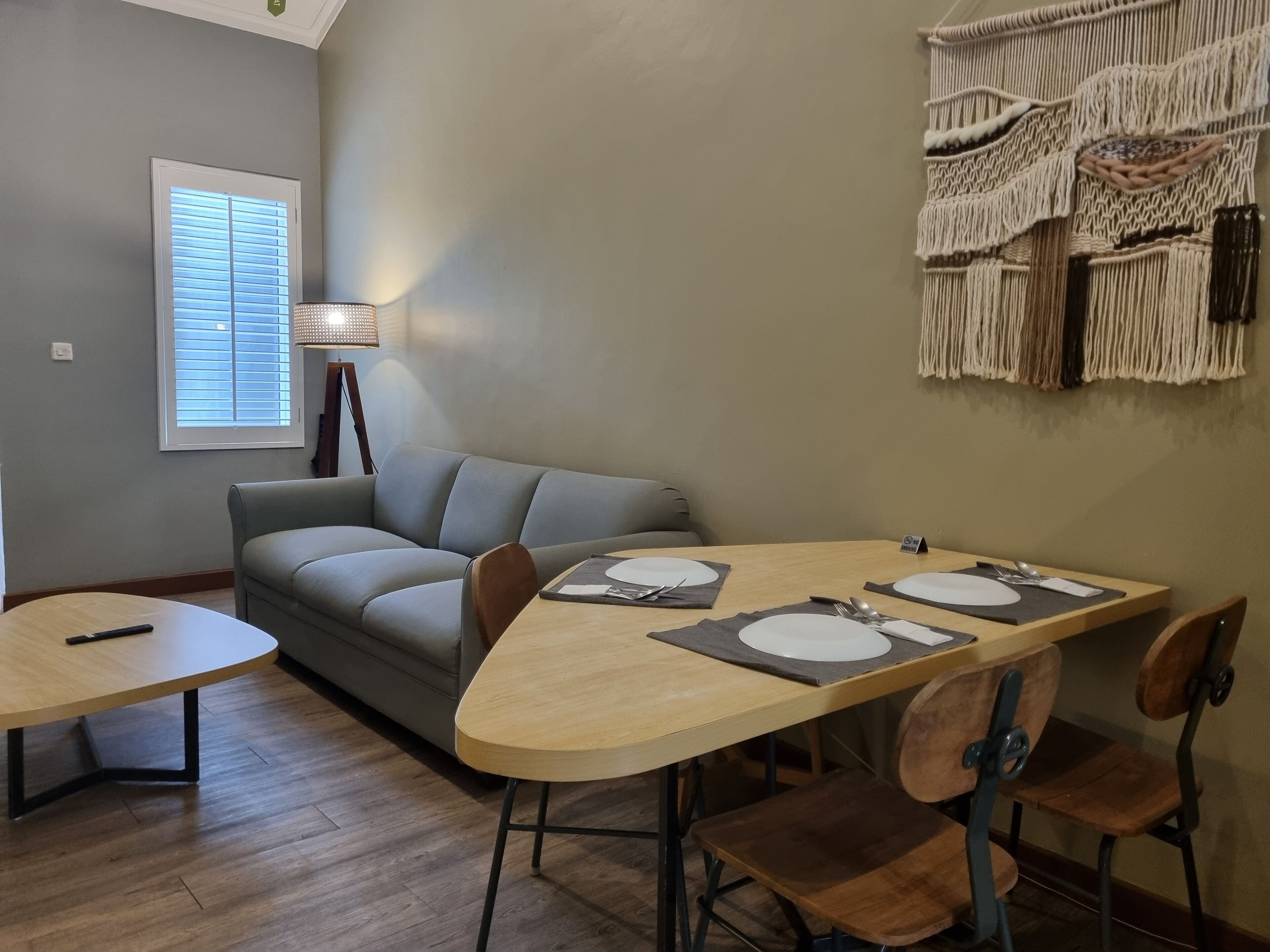 A dining area with a wooden table set for four, a grey sofa, and a macrame wall hanging.