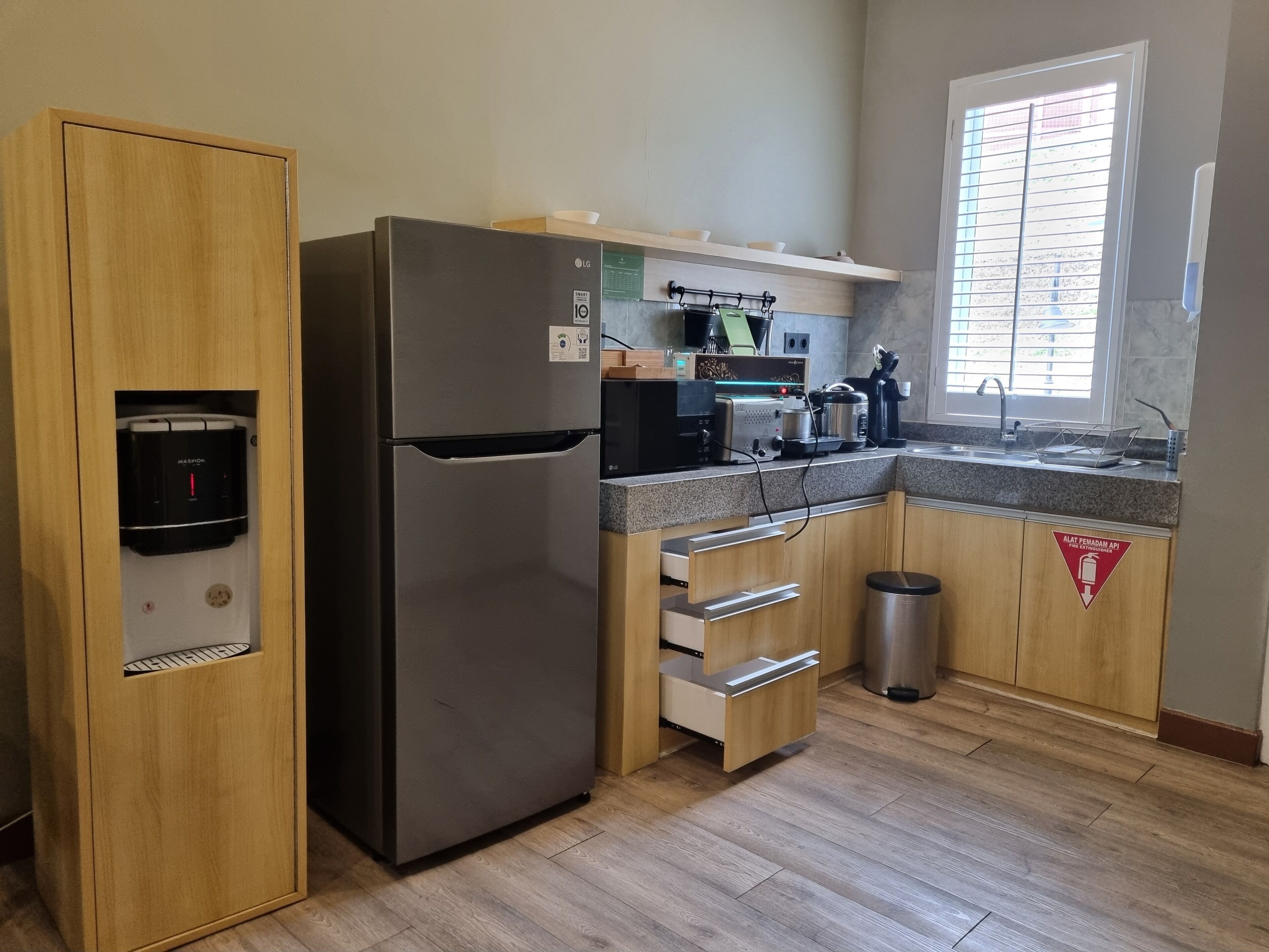 Una cocina moderna con un refrigerador de acero inoxidable, armarios de madera, dispensador de agua integrado, un microondas y un lavamanos.