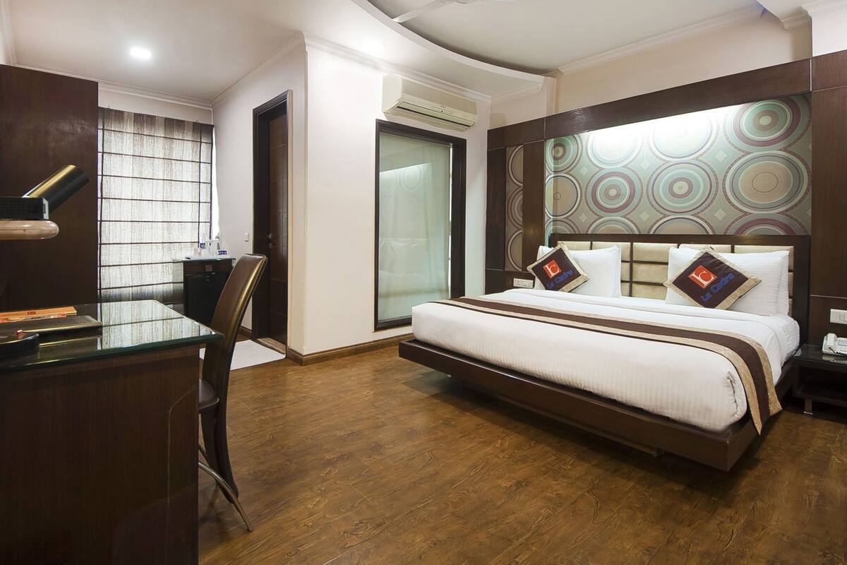 A hotel room with a bed, a desk, a chair, an air conditioning unit, and a patterned wall.