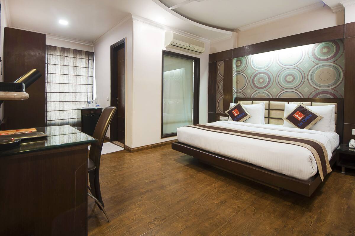 A hotel room with a bed, a desk, a chair, and a window with blinds.