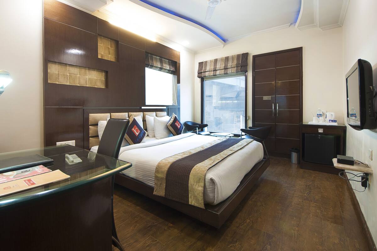A modern hotel room with a large bed, a desk with a lamp, a wardrobe, and a television.