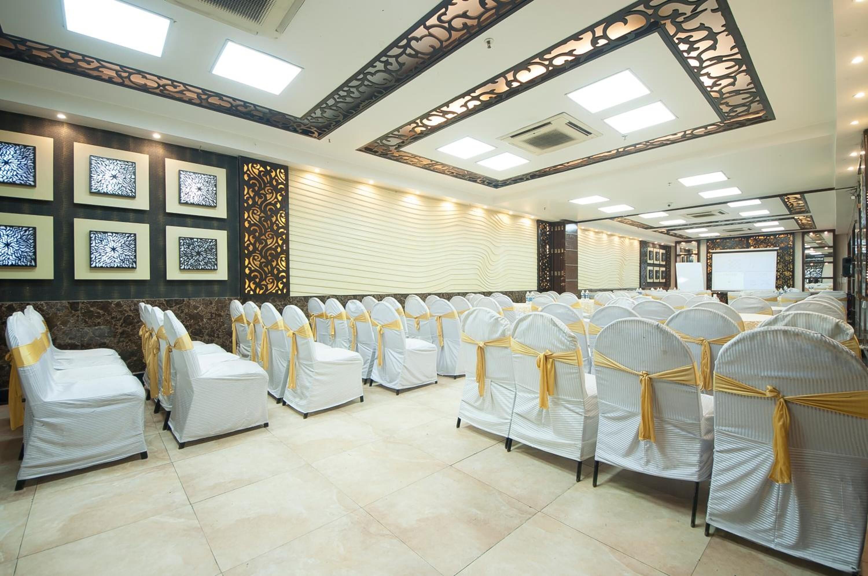 A conference room with rows of chairs covered in white and gold, a large screen, and decorative wall panels.