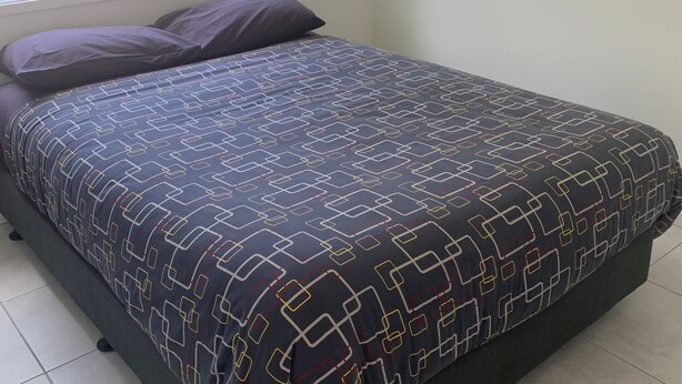 A bed with a geometric patterned bedspread, a window with a view of greenery, and a tiled floor. - Yandina Caravan Park (Sunshine Coast)