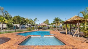 A swimming pool with a brick deck, surrounded by palm trees and a gazebo. - Yandina Caravan Park (Sunshine Coast)