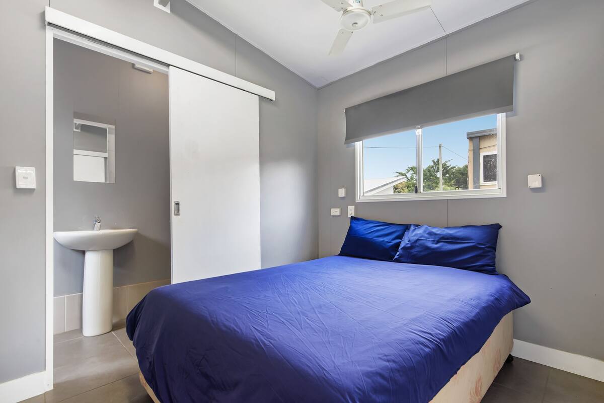 Un dormitorio con cama, ventana, ventilador de techo y baño con lavamanos.