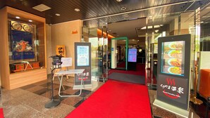A hotel entrance with a red carpet, a reception desk, and digital menu boards.