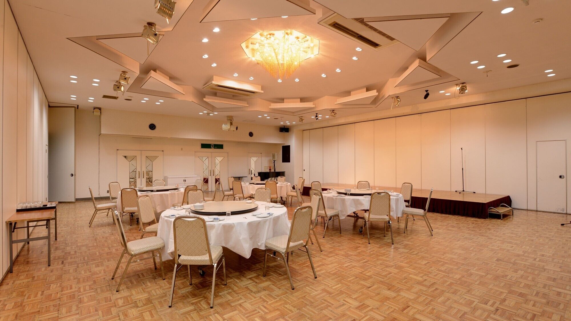 A conference room with round tables, chairs, a stage, and a chandelier.