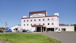 A multi-story building with a flat roof, a central entrance, and a parking area in front.