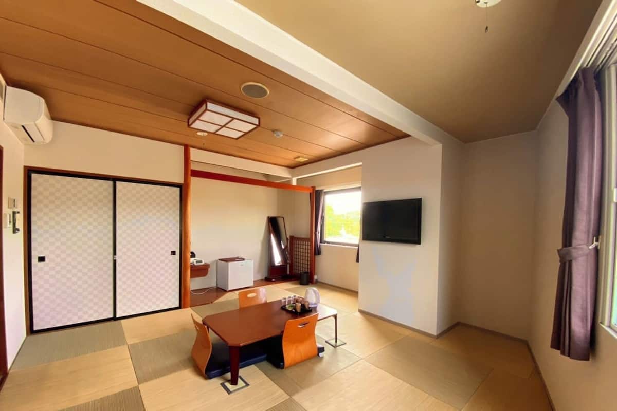 A traditional Japanese room with tatami flooring, a sliding door, a TV, and a desk with a chair.