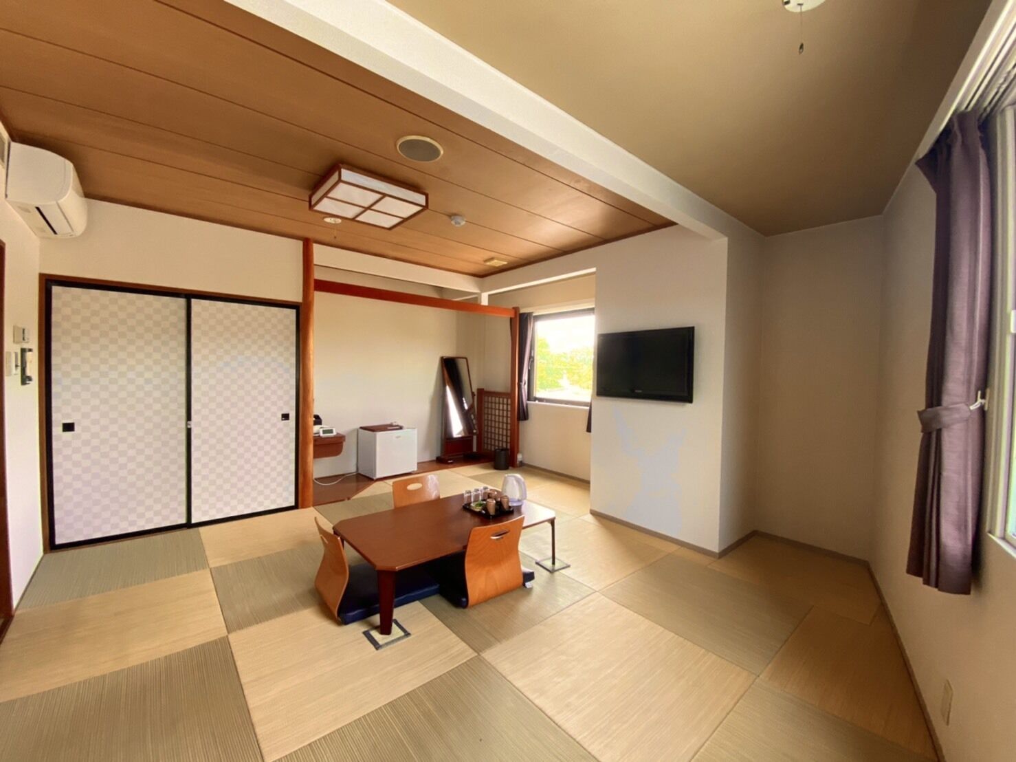 Ein traditioneller japanischer Raum mit Tatami-Boden, einer Schiebetür, einem Fernseher und einem Schreibtisch mit Stuhl.