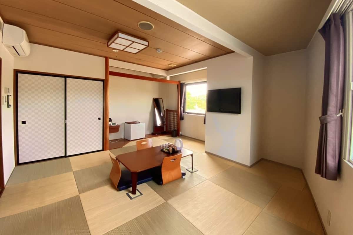 A traditional Japanese room with tatami flooring, a sliding door, a TV, and a desk with a chair.