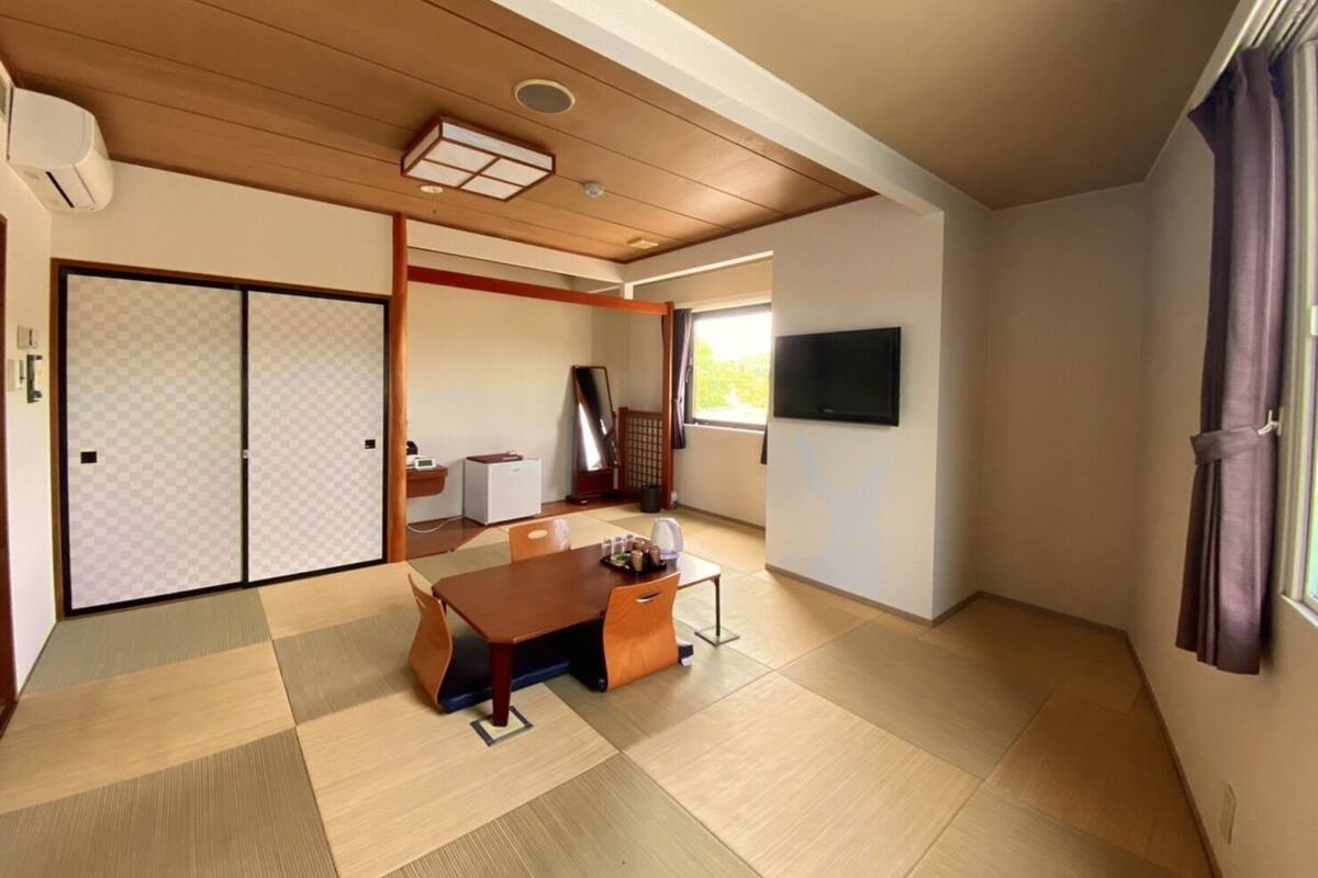 Una habitació japonesa tradicional amb fons de tatami, una porta corredissa, un televisor i una taula amb una cadira.