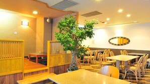 A restaurant interior with wooden furniture, a central plant, and a patterned floor. - First Inn Haiki (Sasebo)