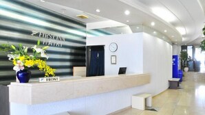 A modern reception desk with a nameplate, a clock, and a vase of flowers. - First Inn Haiki (Sasebo)