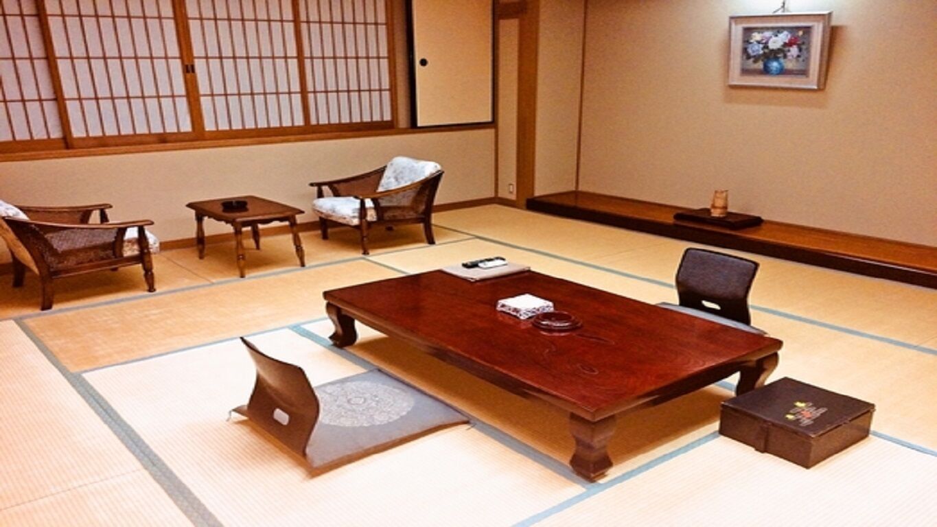 Une pièce de style japonais traditionnel, avec un sol recouvert de tatamis, une table en bois, des chaises et un paravent en papier de riz (shoji).
