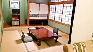 A tatami mat room with a low table and a chair, a futon bed, a TV, and a wardrobe. - Hamasaka Onsen Totoya (Shinonsen)