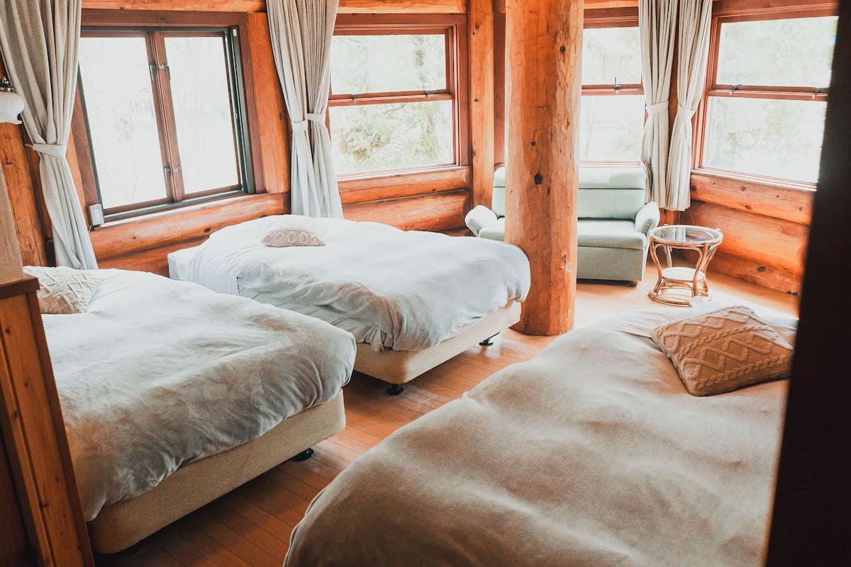 A cozy cabin room with two beds, a small chair, and a window with curtains.