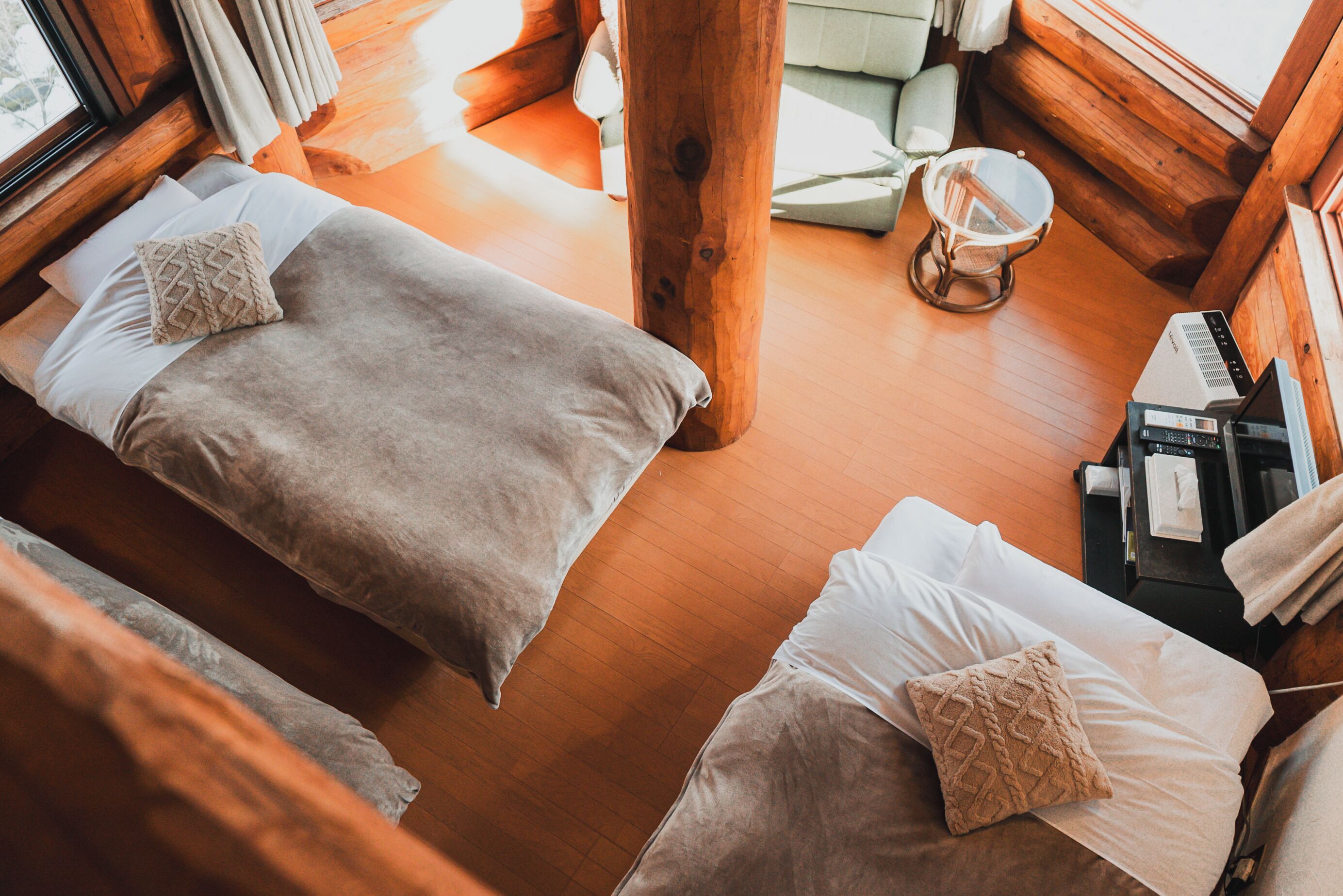 A cozy cabin-style room with two beds, a wooden floor, and a small seating area with a table and chairs.