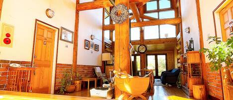 Una habitación amplia con techos altos y vigas de madera, que cuenta con una gran mesa de madera, un sillón amarillo con forma de barco y una chimenea.