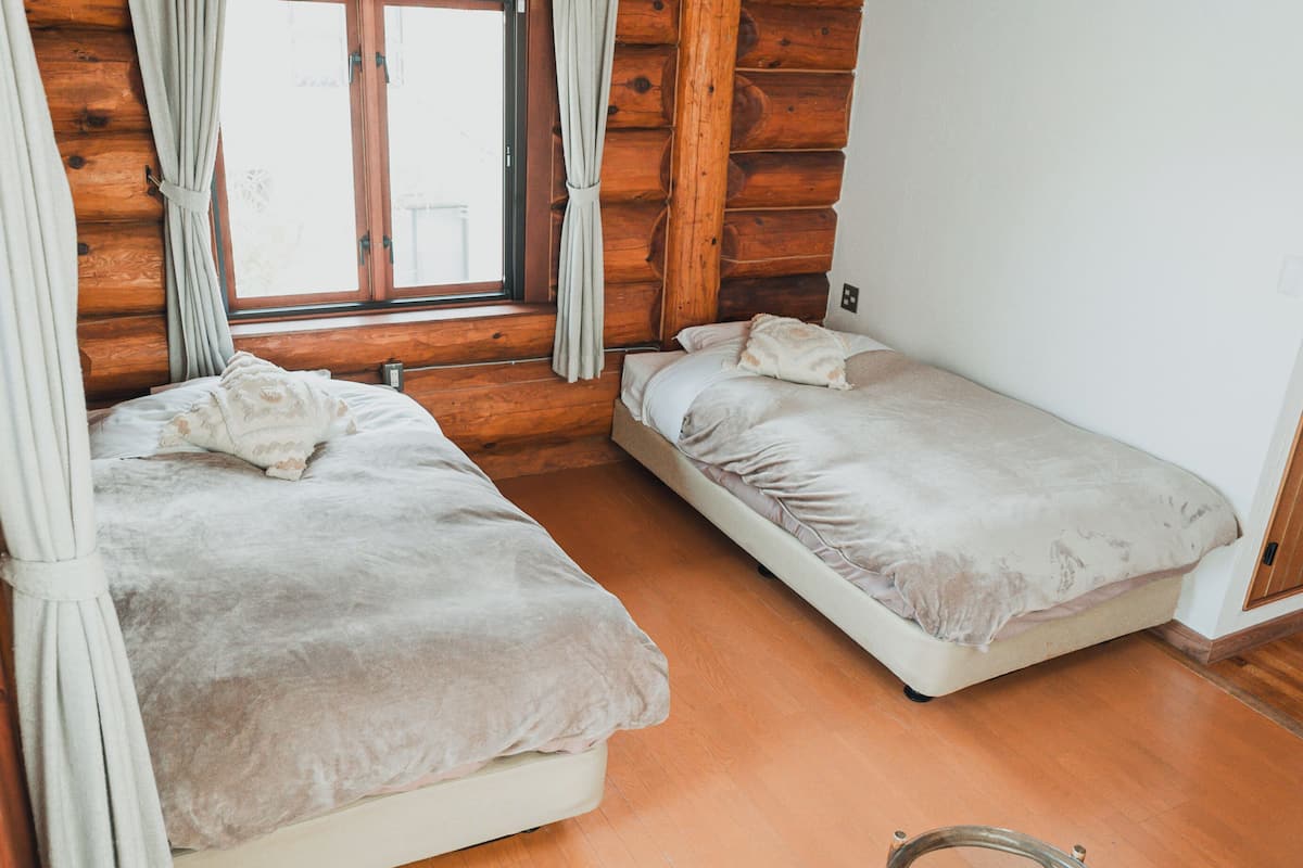 Two single beds in a cabin-style room with wooden walls and a window with curtains.