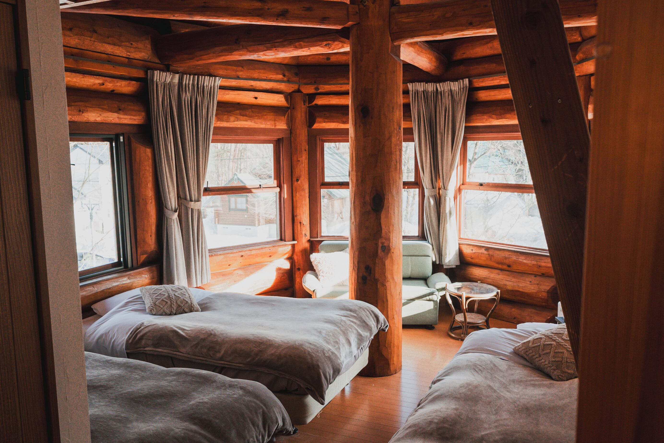 A log cabin room with two beds, a small table, and a chair.
