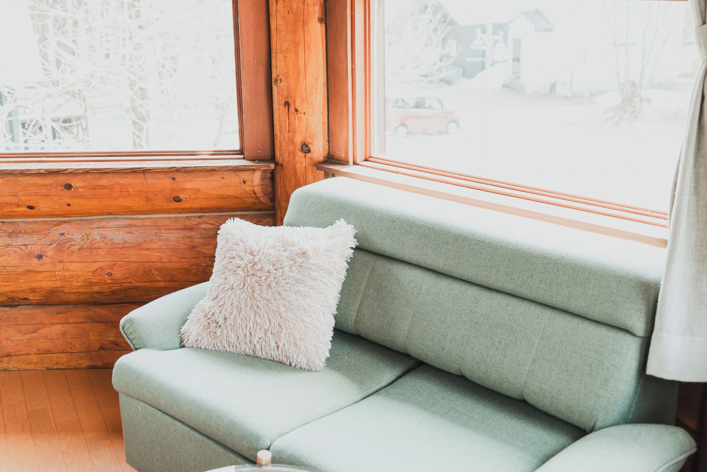 Un canapé vert pâle avec un coussin moelleux, dans une pièce d’une cabane en bois dotée d’une grande fenêtre.