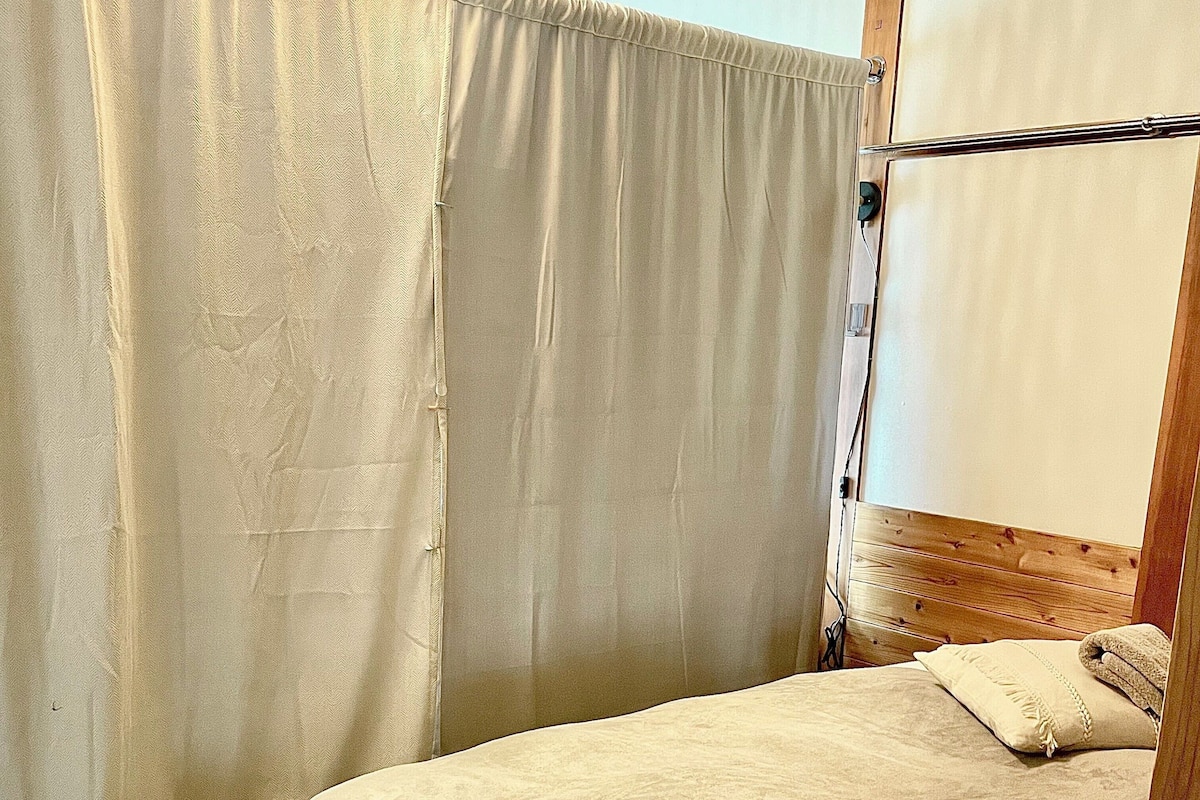 A single bed with a wooden headboard, a beige curtain, and a small bedside table.