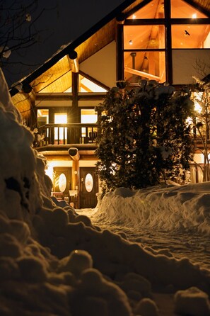 A snow-covered landscape with a wooden building featuring large windows and a balcony. - Hakuba Pension Meteor (Hakuba)