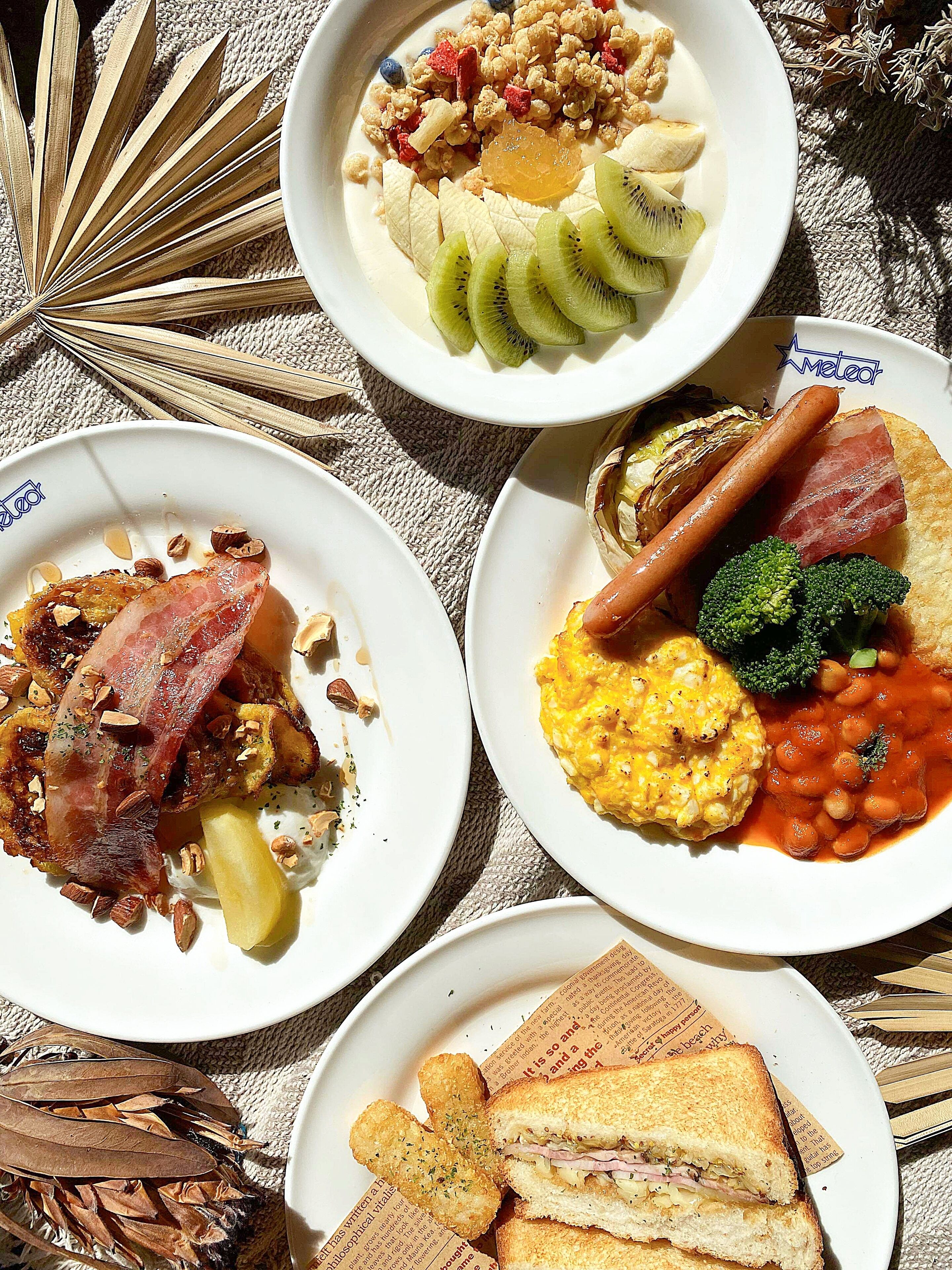 Quatro pratos de comida com diversos itens de café da manhã, incluindo ovos, bacon e vegetais.