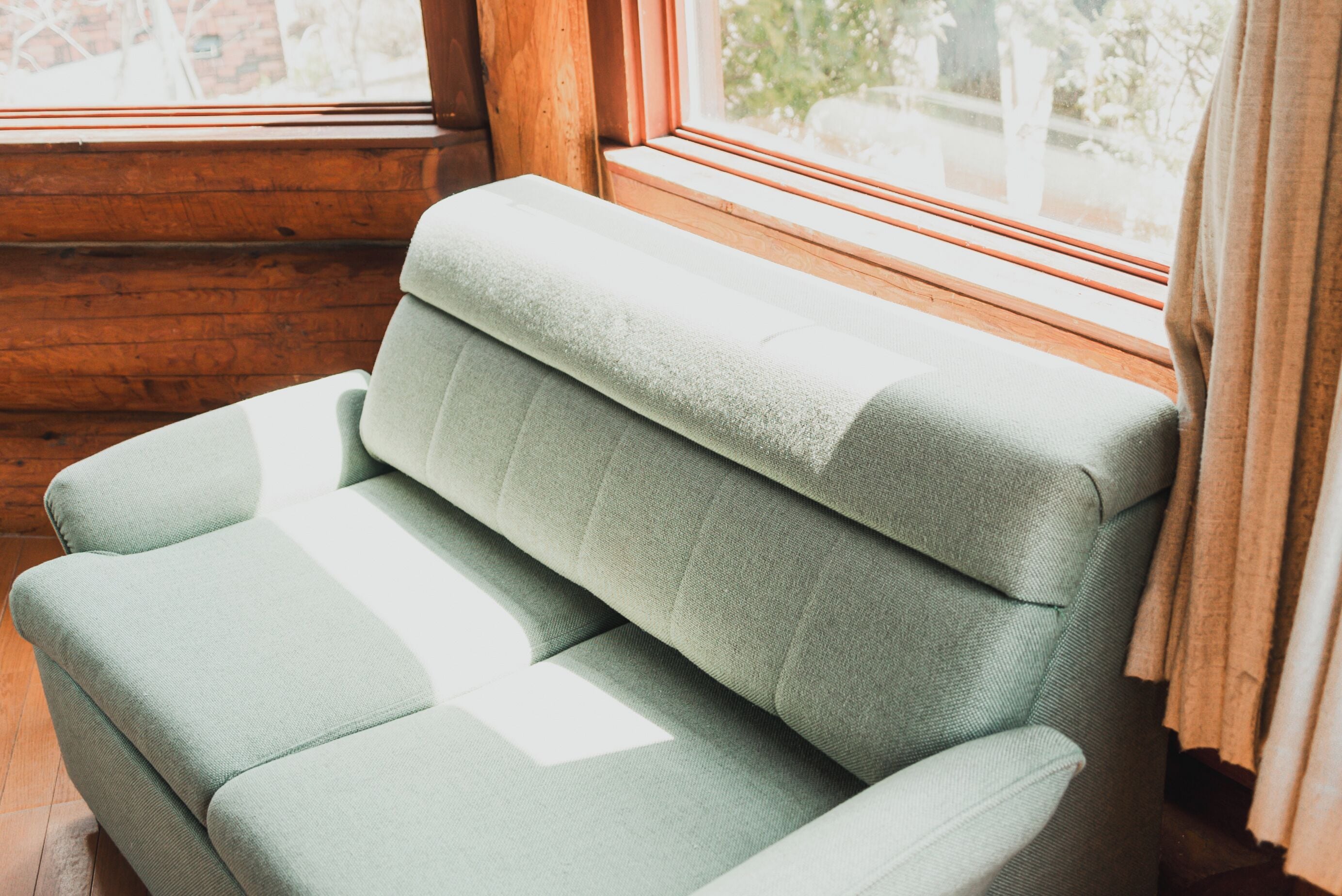 A green upholstered sofa in a room with wooden walls and a window.