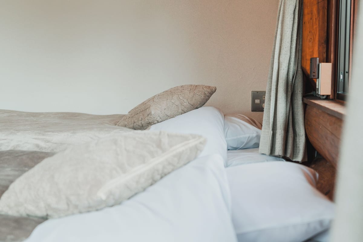 A bed with white and gray bedding, a wooden headboard, and a window with curtains.