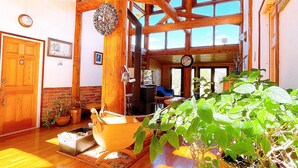 A spacious room with wooden beams, a large window, and a potted plant. - Hakuba Pension Meteor (Hakuba)
