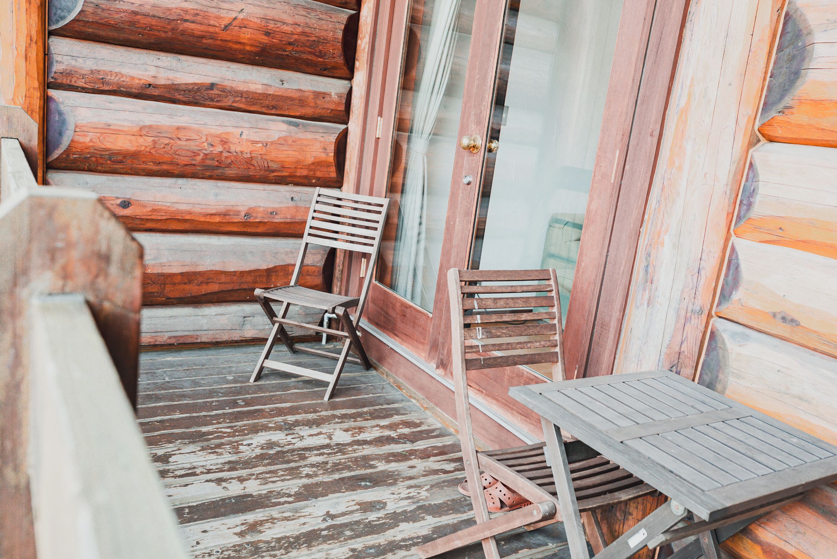 A wooden cabin with a porch, two wooden chairs, and a table.