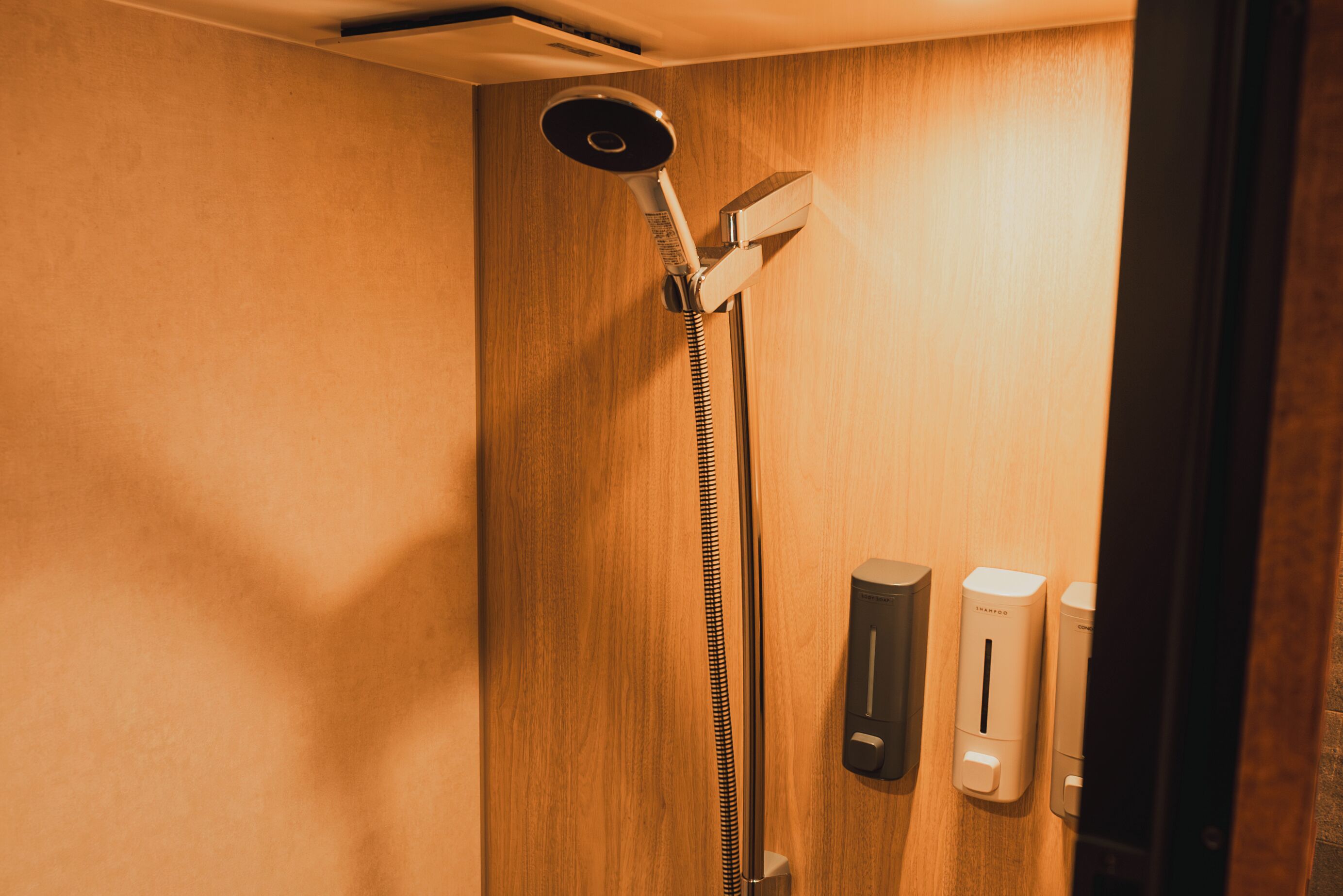 A wooden shower enclosure with a handheld showerhead and two soap dispensers.